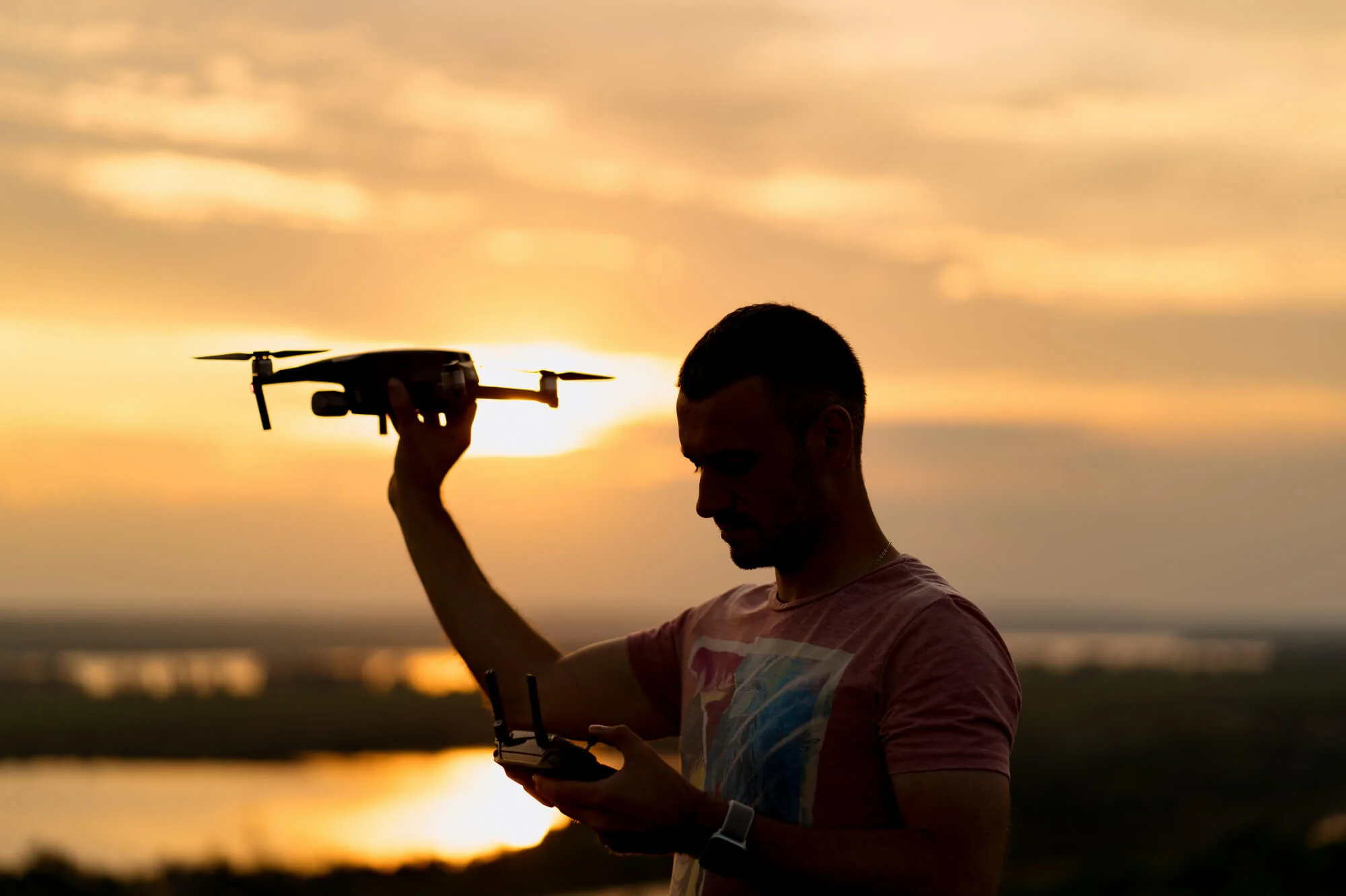Hombre sujetando un dron con una puesta de sol de fondo
