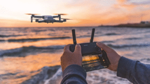 Persona controlando un dron en la costa al atardecer