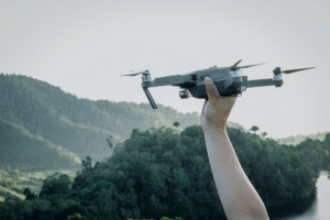 persona alzando un dron con la mano con montañas y pinos de fondo