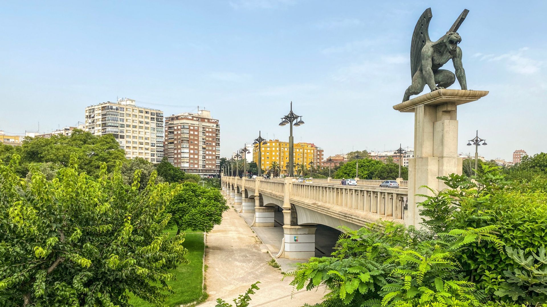 parque de valencia, se ven árboles, un puente y una estatua con edificios de fondo